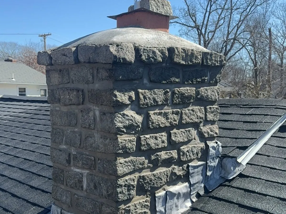 Brick and stone chimney with fresh mortar and new flashing on a shingled roof